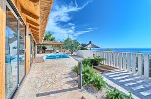 A wooden villa with a pool, a covered patio, and a view of the sea.