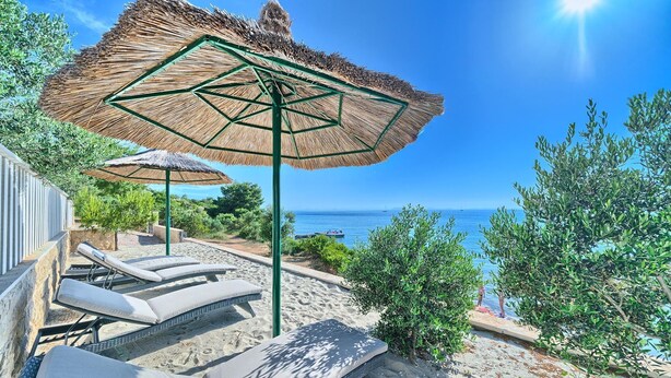 Zona relax a la platja amb gandules i paraigües de palla, amb vista a un mar blau i translúcid.