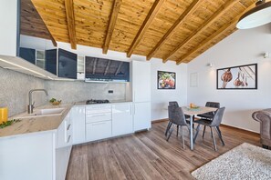 A modern kitchen with white cabinets, a wooden ceiling, and a dining area with a table and chairs.