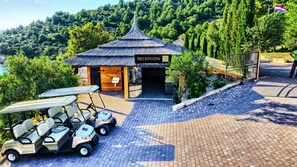 A reception building with a thatched roof, a sign reading "RECEPCION", and a view of the surrounding greenery and hills.