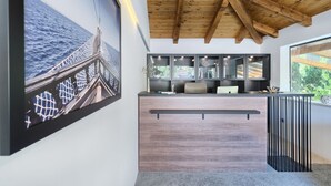A modern reception desk with a wooden finish, a large framed photograph of a bridge, and a view of greenery through a window. - Luxury Glamp New Horizons V (Murter)