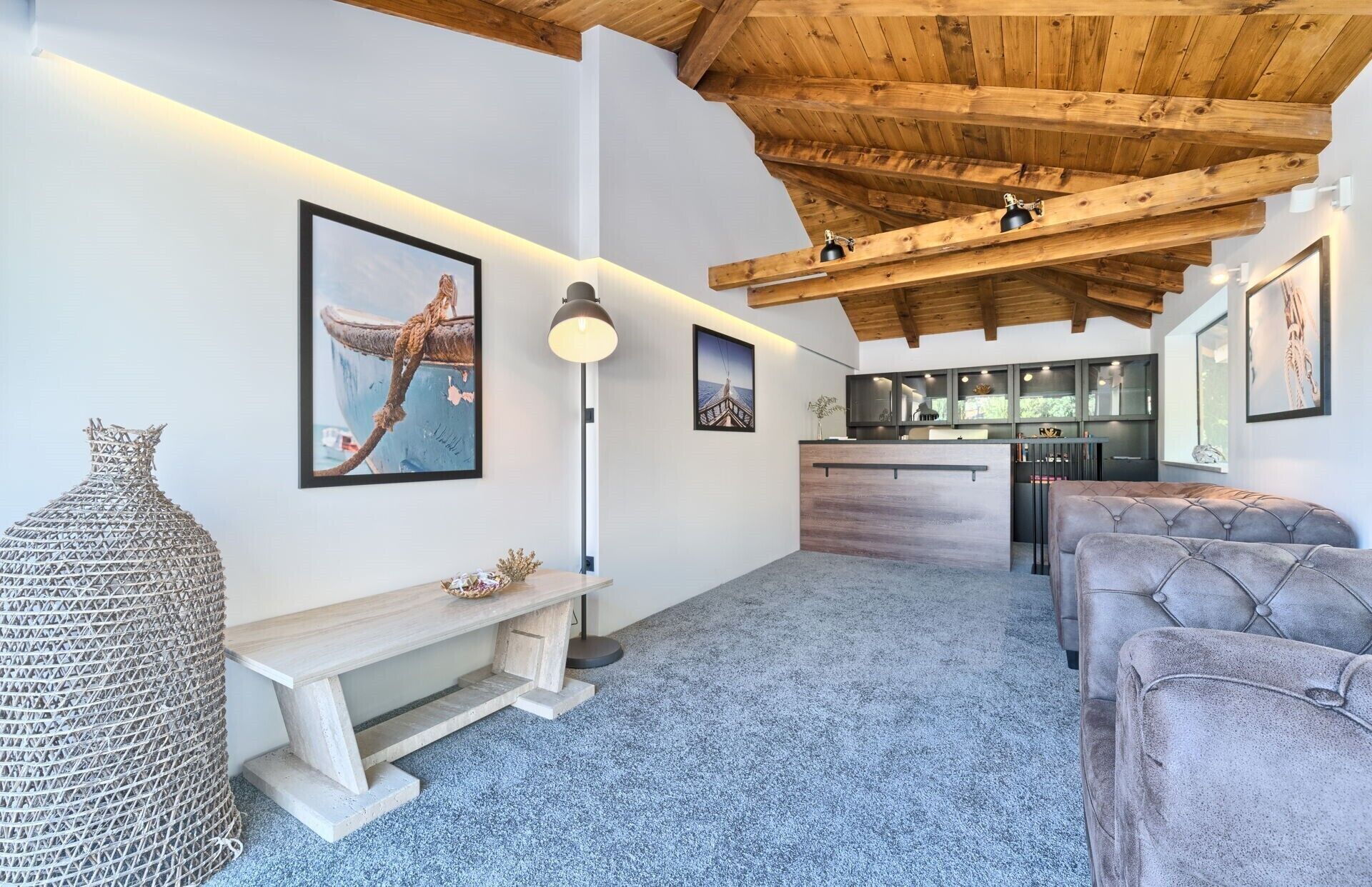A modern interior with a wooden ceiling, a bench, a sofa, and a kitchen area.