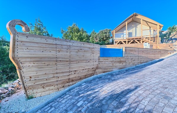A wooden boat-shaped structure with a blue pool, a wooden deck, and a building with a sloped roof. - Luxury Glamp New Horizons II (Murter)