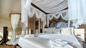 A four-poster canopy bed with white linens and towels, a wooden bench, and a view of the room's decor. - Luxury Glamp New Horizons II (Murter)
