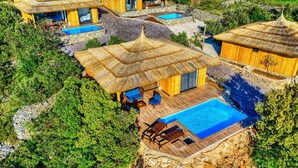 Ein Resort mit mehreren Bungalows mit Strohdach, einem zentralen Poolbereich und umgebender Vegetation.
