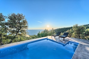 A swimming pool with two lounge chairs and a view of the sea.