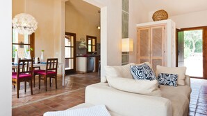 Un grand espace de vie comprenant un canapé, des fauteuils et une table à manger. On aperçoit une cuisine au fond.