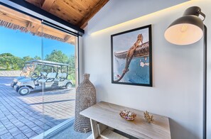 A room with a large window, a framed painting, a table with decorative items, and a golf cart outside.