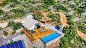 A modern outdoor accommodation with a wooden deck, a swimming pool, and a thatched-roof structure.