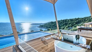 A luxurious outdoor setting with a wooden deck, a hot tub, and a view of a large body of water and a forested hillside. - Luxury Glamp New Horizons I (Murter)