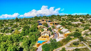 Une propriété située sur une colline, comprenant plusieurs chalets en bois, une piscine et un ciel d’un bleu éclatant.