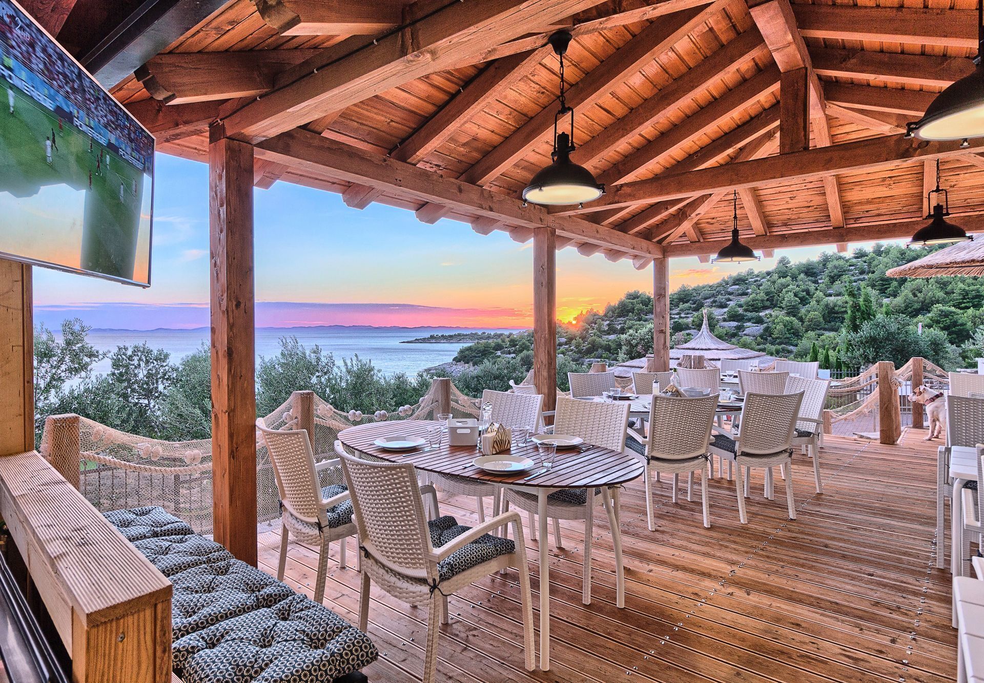 Une terrasse en bois avec des sièges extérieurs et une vue sur la mer au coucher du soleil.
