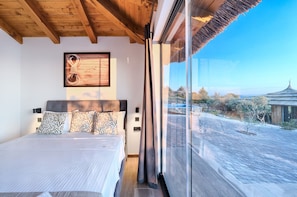 Un dormitorio con una cama grande, techo de madera, un cuadro enmarcado en la pared y vistas a un patio con un edificio tradicional.