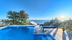 Ein Pool mit zwei Liegestühlen, einem Baum und Blick aufs Meer.