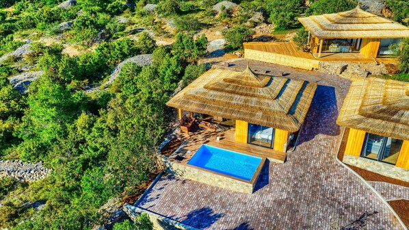 Un resort con varias construcciones de techo de paja, una piscina y abundante vegetación alrededor de los edificios.