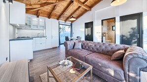 Ein modernes Interieur mit Holzbalkendecke, einem Wohnbereich mit Sofa, einem Glastisch und einer Küche mit weißen Schränken.