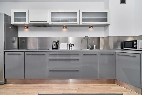 Une cuisine moderne avec des meubles gris, des appareils en acier inoxydable et un four à micro-ondes.