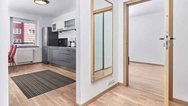 A modern kitchen with grey cabinets, a stainless steel refrigerator, and a window with a view of a red building.