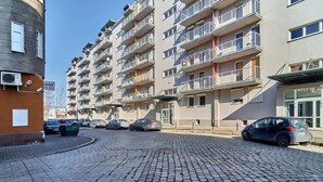 A multi-story residential building with balconies, a paved street, and parked cars.