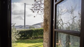 Una ventana con vistas a un césped, un muro de piedra y un paisaje lejano con colinas.