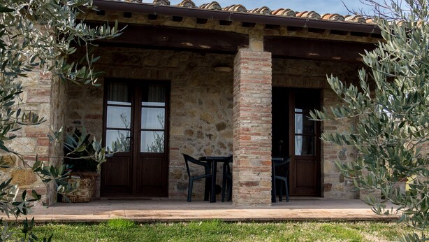 Un edificio de piedra con techo de tejas, dos puertas y un pequeño espacio al aire libre con sillas y mesas.