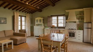 Una amplia sala de estar con una mesa y sillas de madera, un sofá y una cocina con armarios blancos y una estufa.