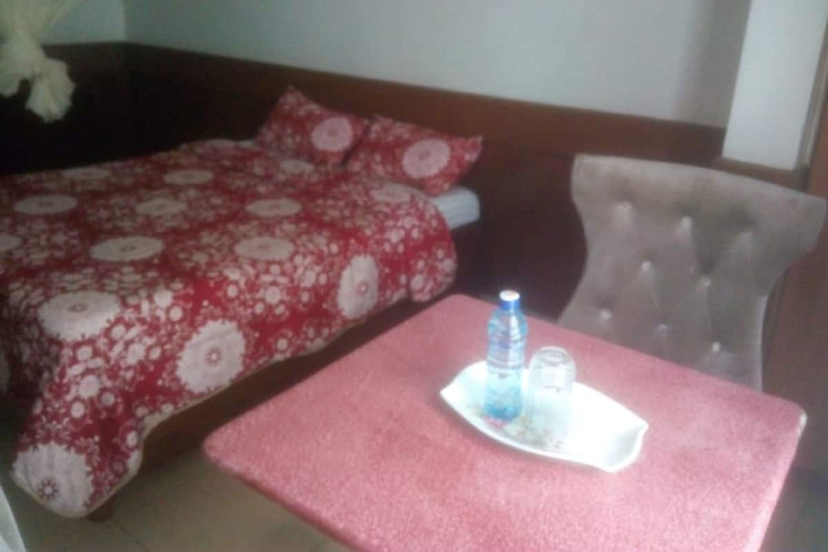 A hotel room with a bed, a chair, and a table with a water bottle and glasses.