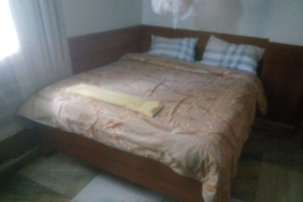 A bed with a patterned bedspread and pillows, a wooden headboard, and a window with curtains.