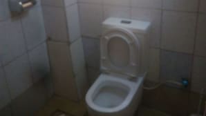 Et lille badeværelse med fliser, toilet, en lille hylde og et vindue med naturligt lys.