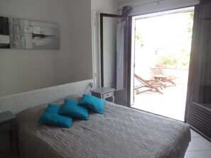 Un dormitorio con cama, mesita de noche, ventana y vista a un área de estar exterior.