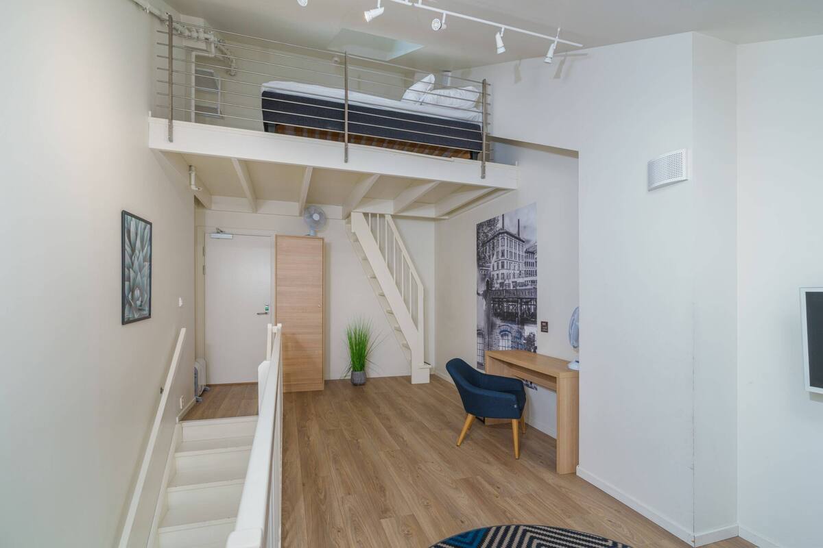 A loft bedroom with a bunk bed, a desk, a chair, a staircase, and a potted plant.