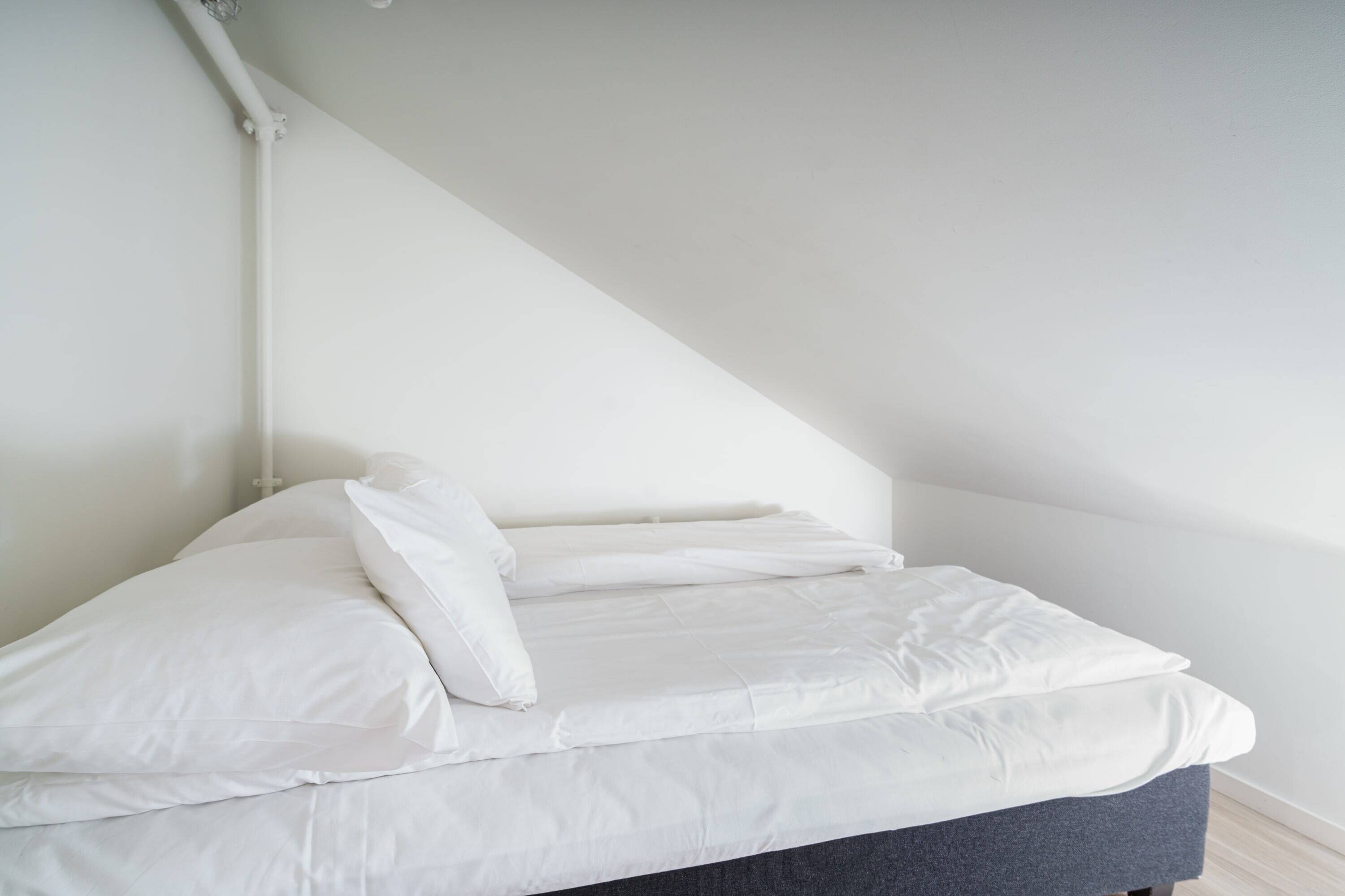 Ein Bett mit weißer Bettwäsche in einem Zimmer mit weißen Wänden und einer geneigten Decke.