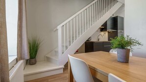 Una cocina moderna con armarios blancos, una mesa de comedor de madera y una escalera con barandillas blancas.