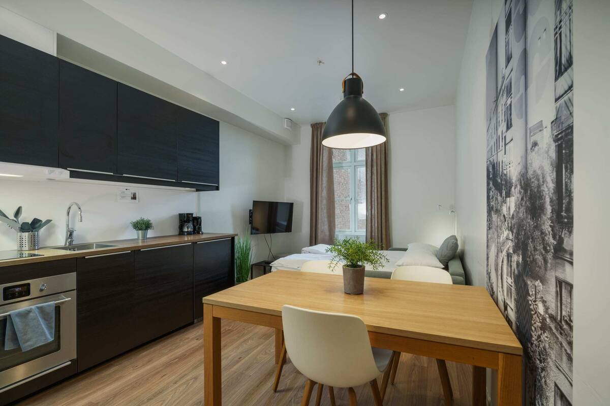 A compact hotel room with a kitchenette, a dining area, a bed with a view, and a large window.