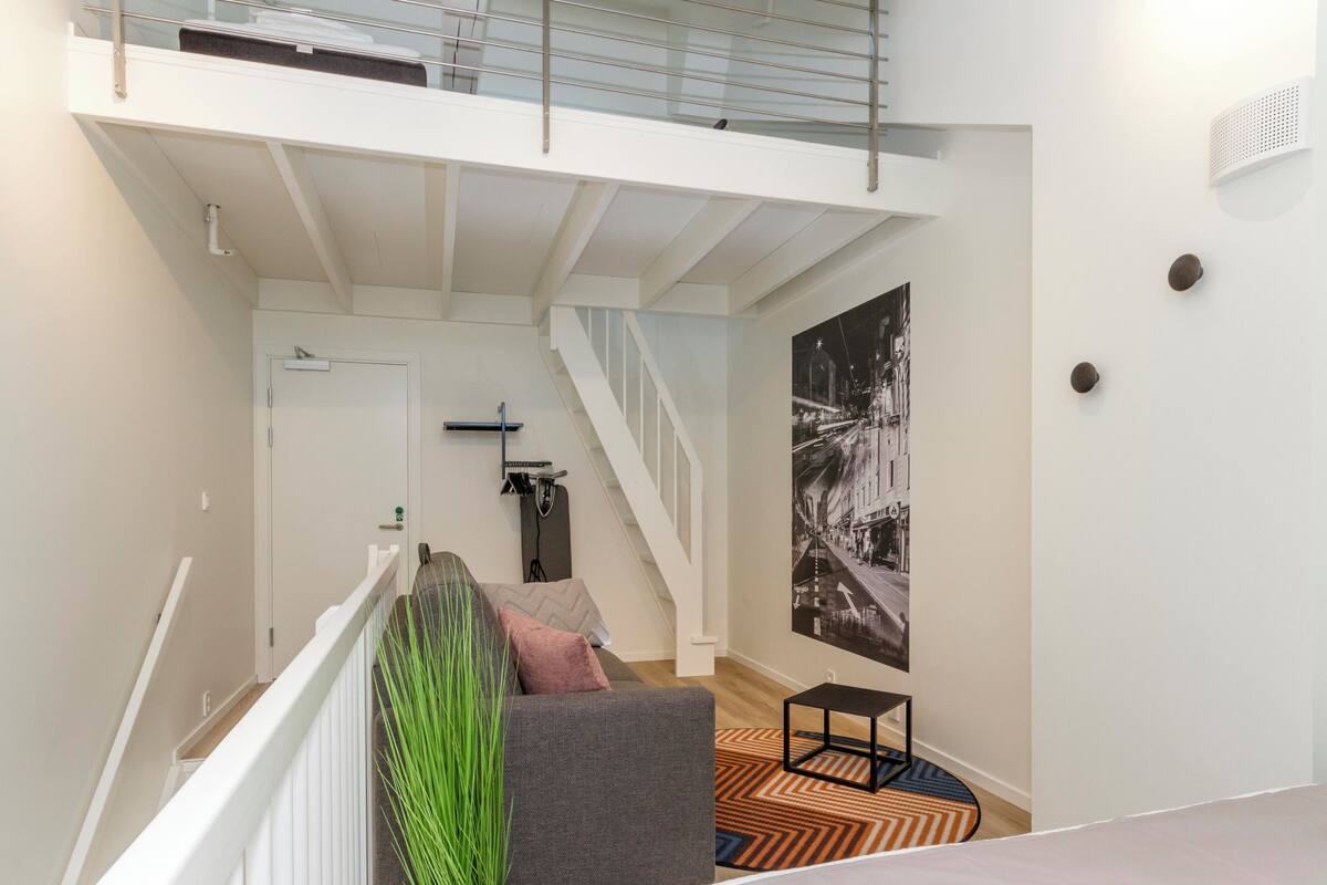 A modern interior with a staircase, a grey sofa, a small table, and a poster on the wall.