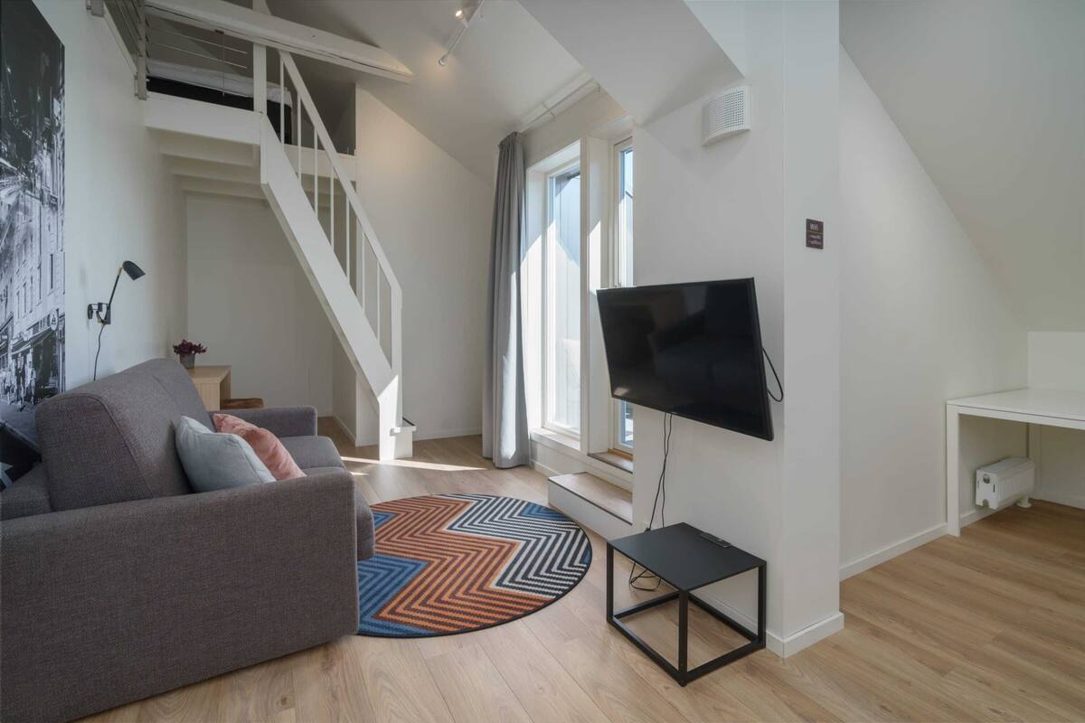 A modern living room with a sofa, a TV, a staircase, and a large window.