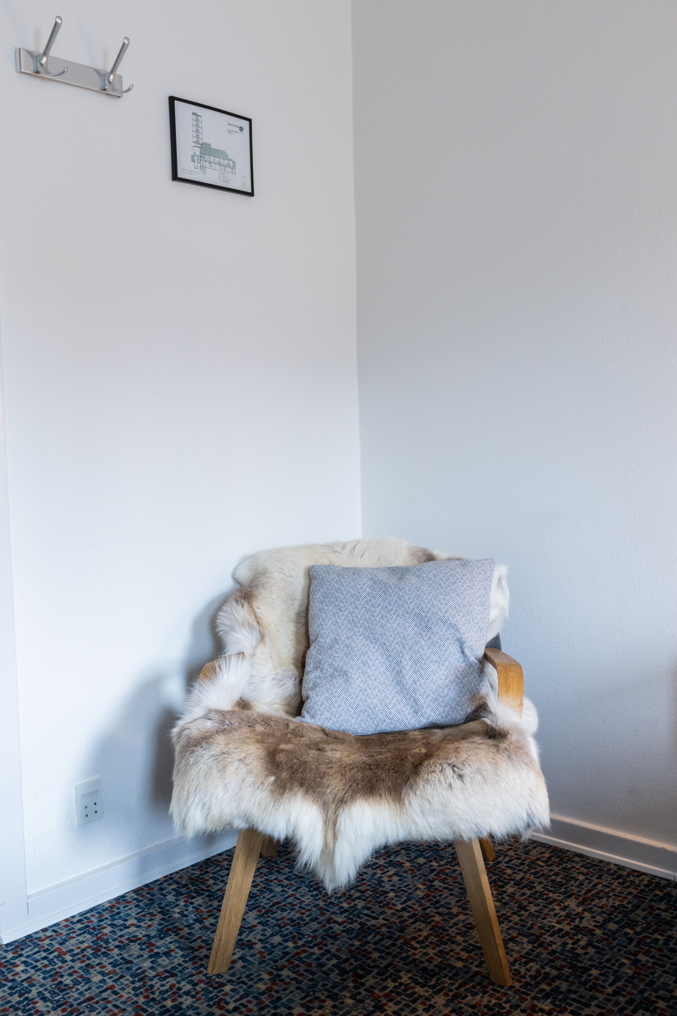 A chair with a fur seat and a cushion, a wall-mounted light fixture, and a framed architectural drawing on the wall.