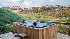 Eine Holzdiele mit Whirlpool und Treppe, die zu ihm hinaufführt, mit Blick auf eine malerische Landschaft mit bunten Häusern.
