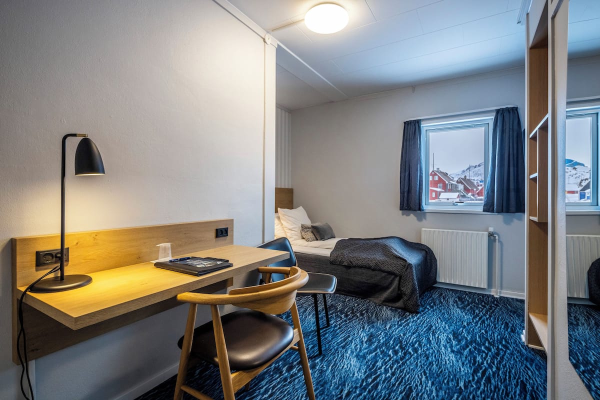Een hotelkamer met een bureau, stoel, bed en een raam met gordijnen.