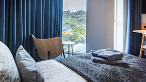 Ein Hotelzimmer mit Bett, Stuhl, kleinem Tisch und Blick auf eine gebirgige Landschaft.