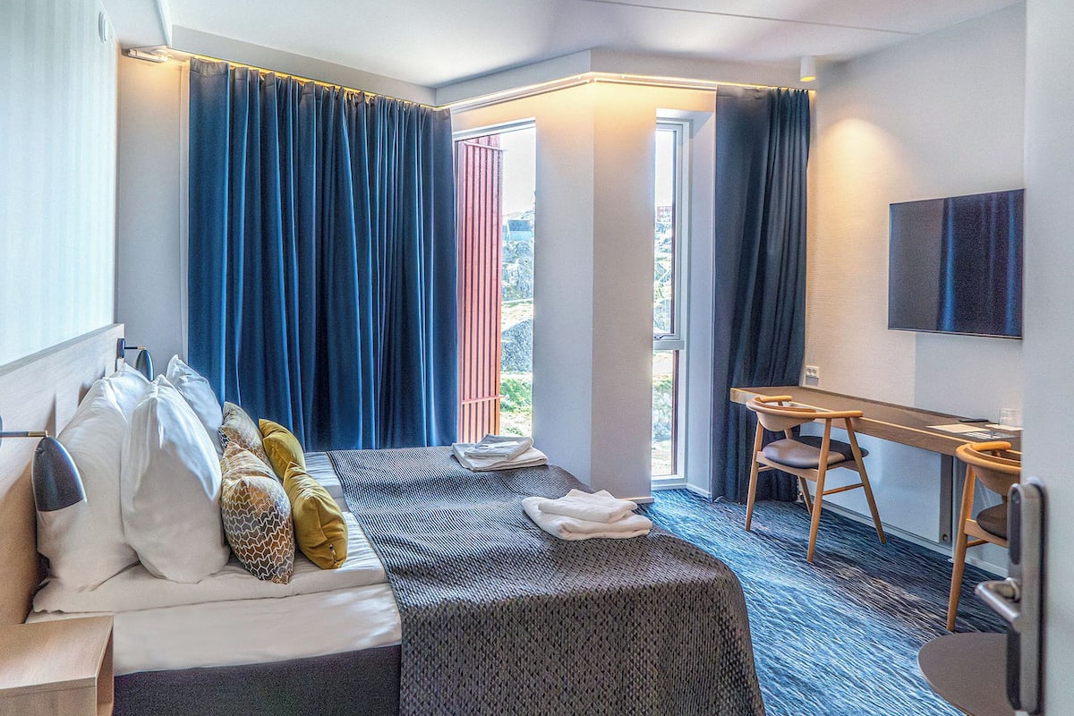 Een hotelkamer met een bed, een bureau, een stoel en een groot raam met gordijnen.