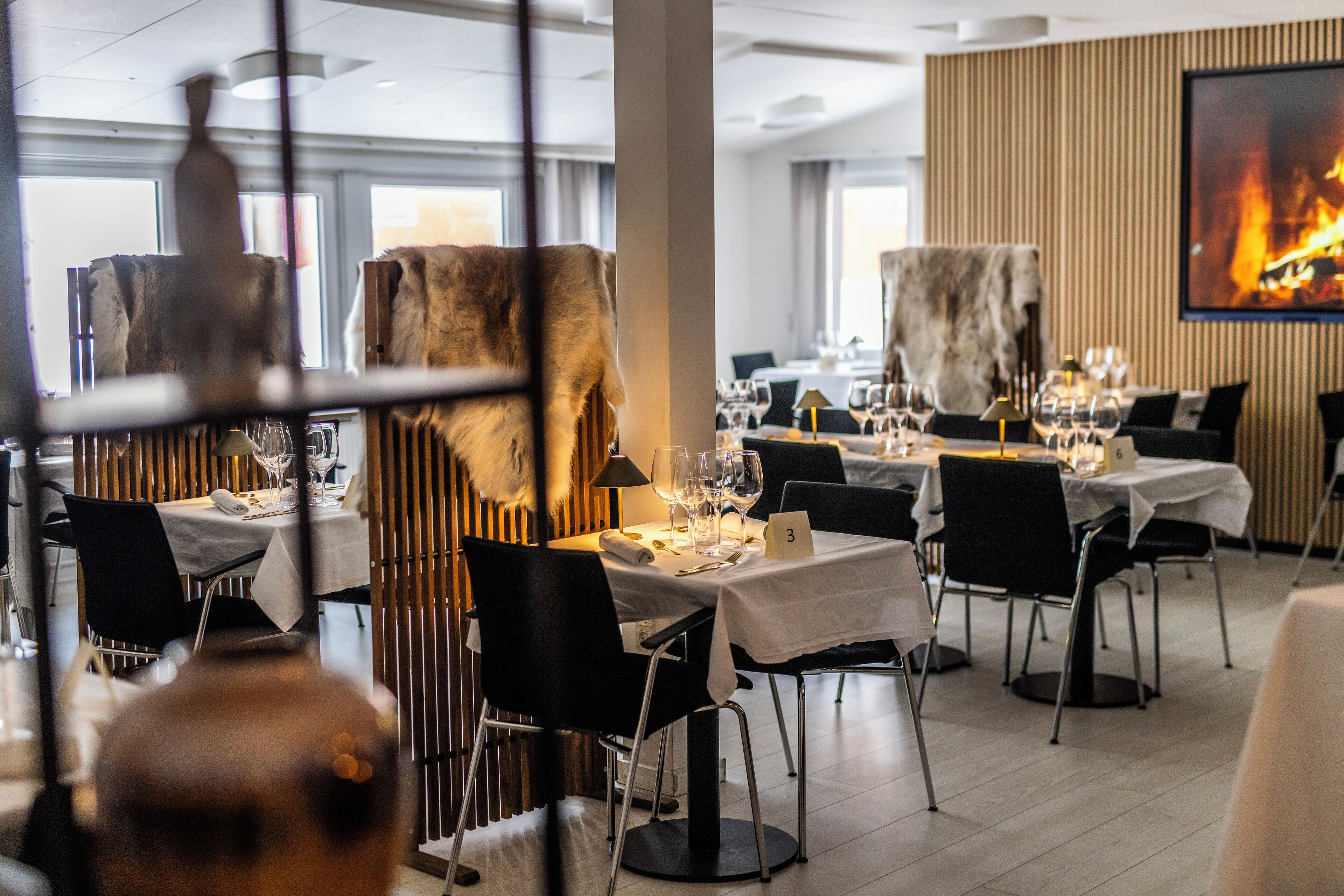 Un restaurant avec des tables dressées pour le service, un grand tableau accroché au mur et une vue sur l’extérieur.