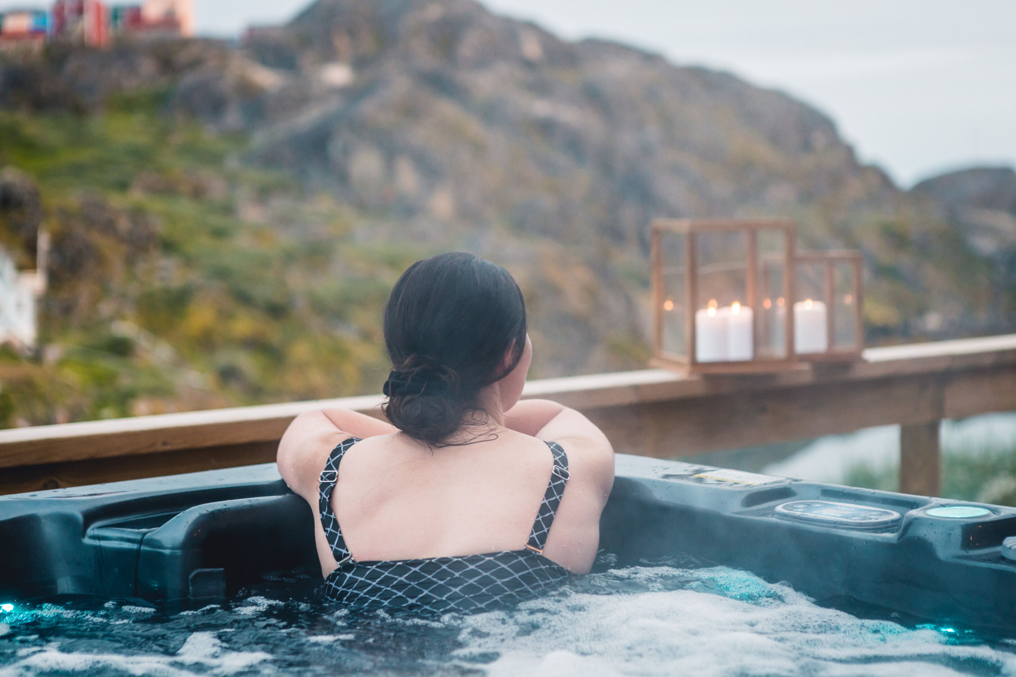 A person in a hot tub with a view of mountains and a wooden deck.