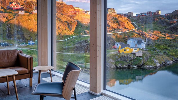Ein modernes Interieur mit einem großen Fenster, das einen malerischen Blick auf ein Küstendorf und einen Fluss bietet.