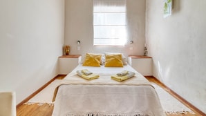 Quarto com cama, duas mesas de cabeceira, uma janela e luminária na parede.
