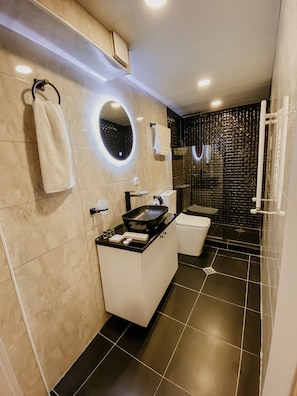 Un baño moderno con tocador blanco y negro, un espejo redondo y una zona de ducha con azulejos negros.