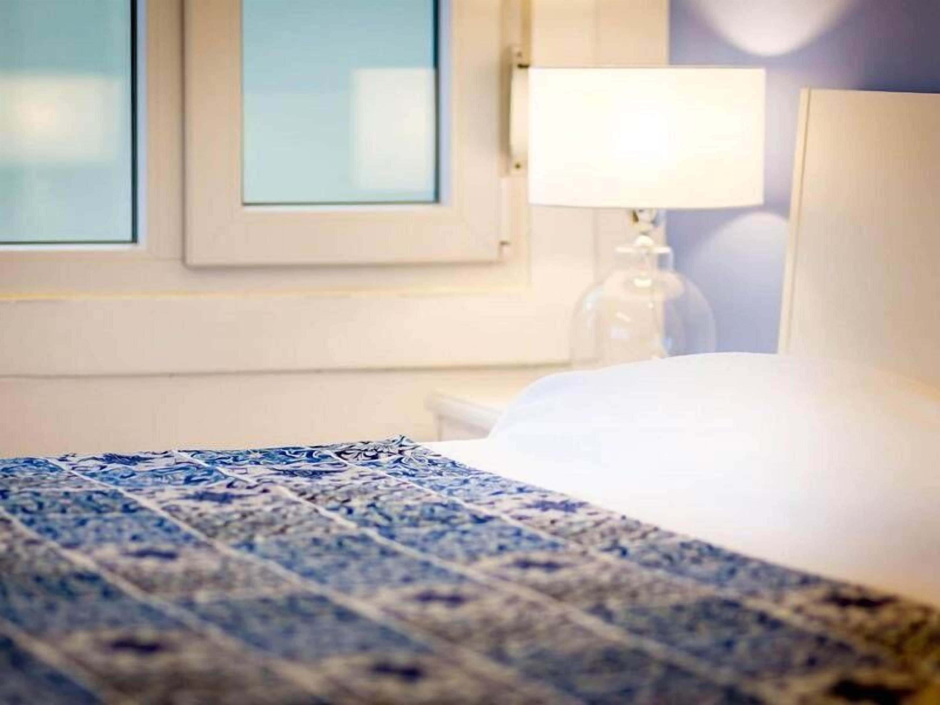Una habitación de hotel con cama, mesita de noche, lámpara y ventana.