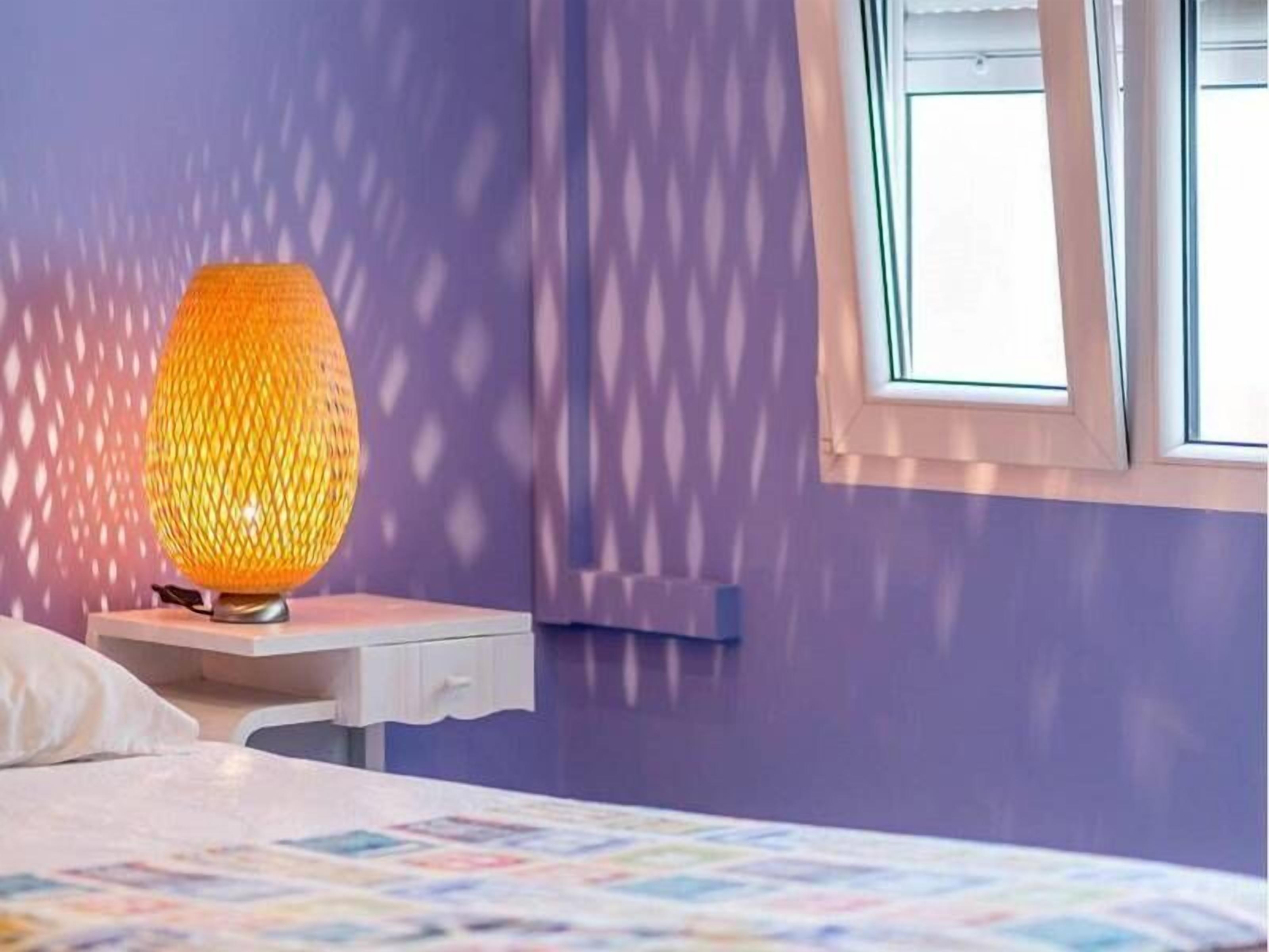 A bedroom with a bed, a nightstand, a lamp, and a window with blinds.