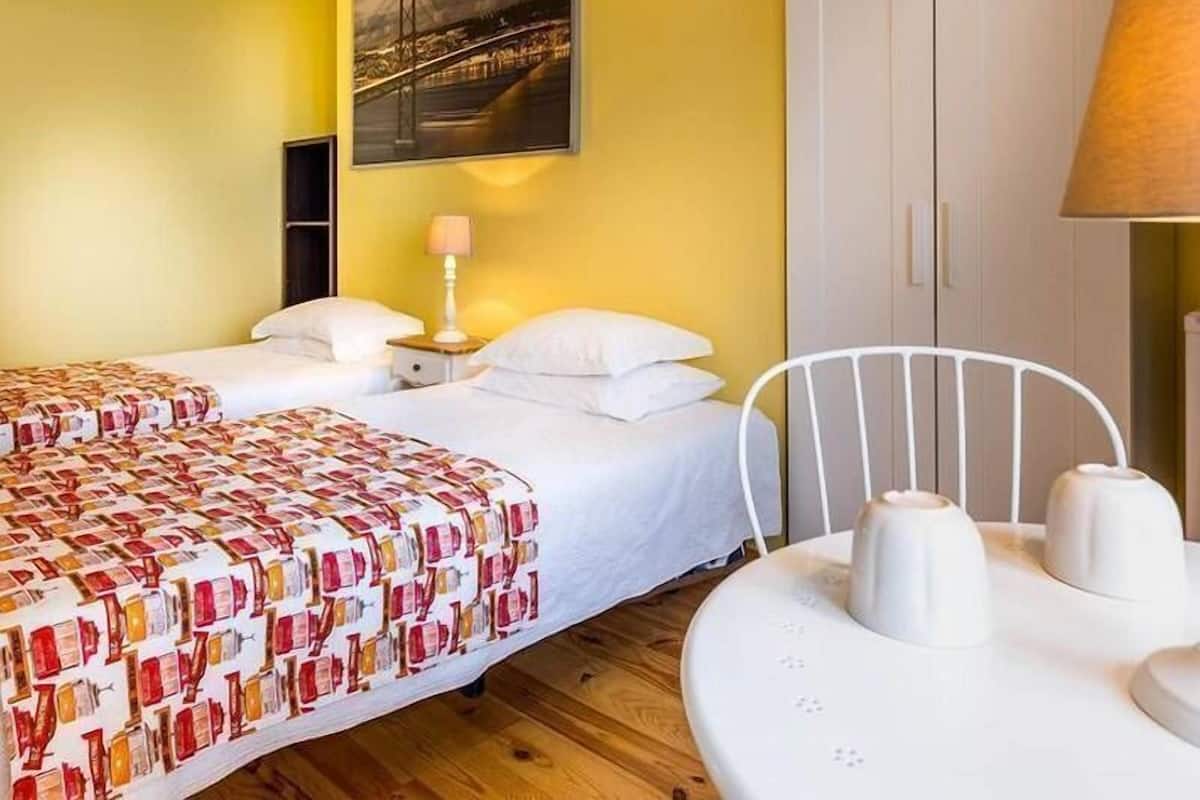 Una habitación de hotel con dos camas, una mesa de comedor con sillas, una lámpara y un cuadro de un puente en la pared.