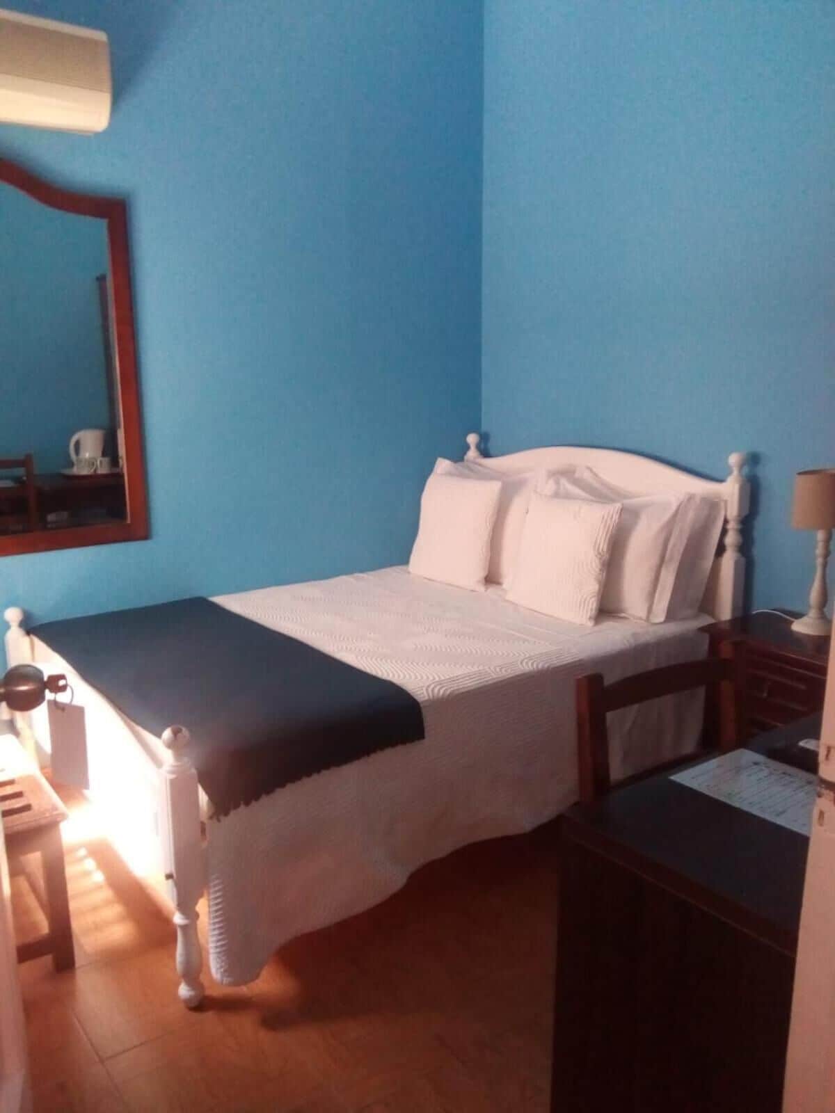 A bedroom with a bed, a desk, a chair, a lamp, and a mirror.